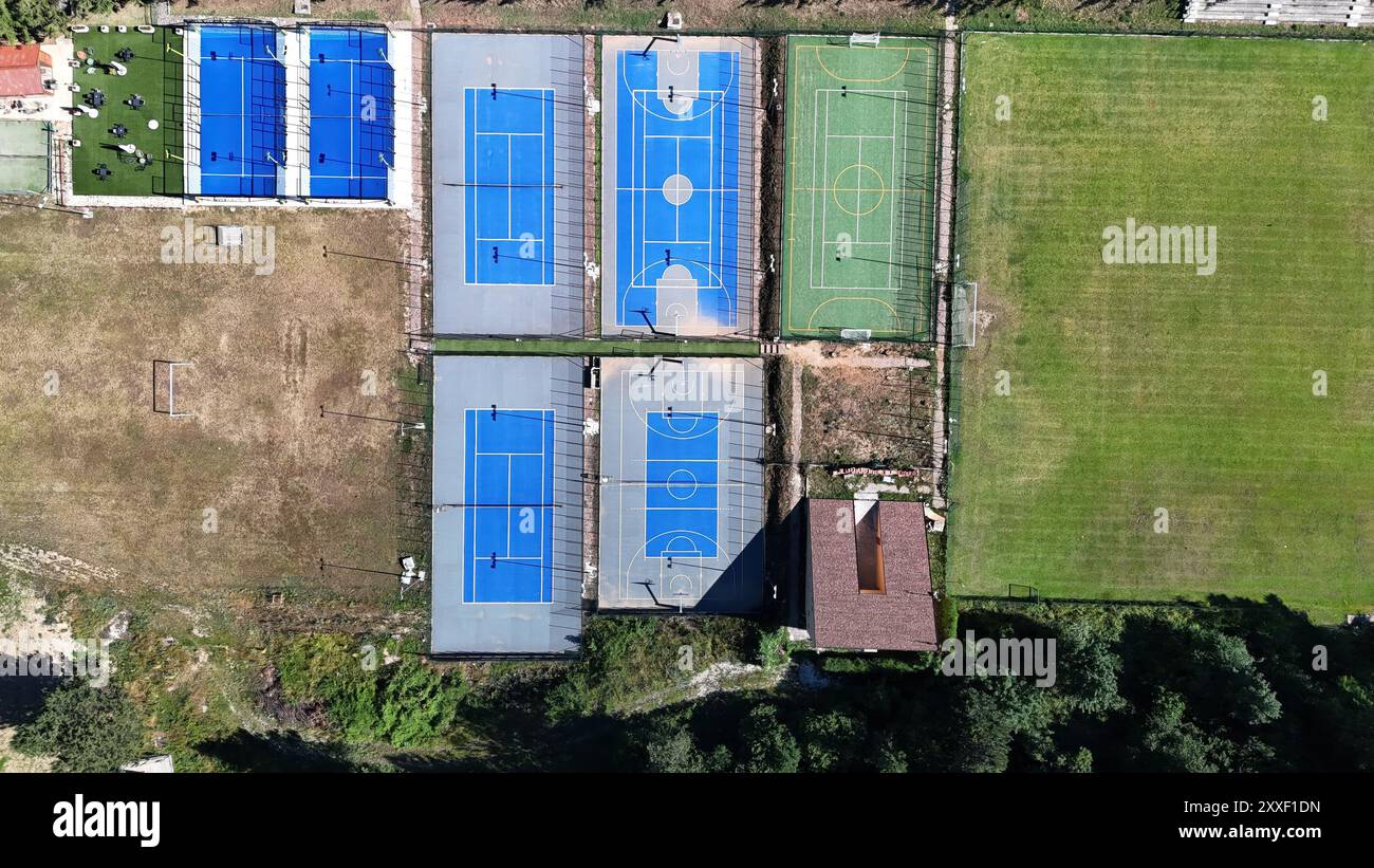 Aus der Vogelperspektive zeigt eine Reihe von lebhaften blauen Tennis- und Basketballplätzen, ergänzt durch weitläufige grüne Felder, die alle vor klarem Himmel liegen. Stockfoto