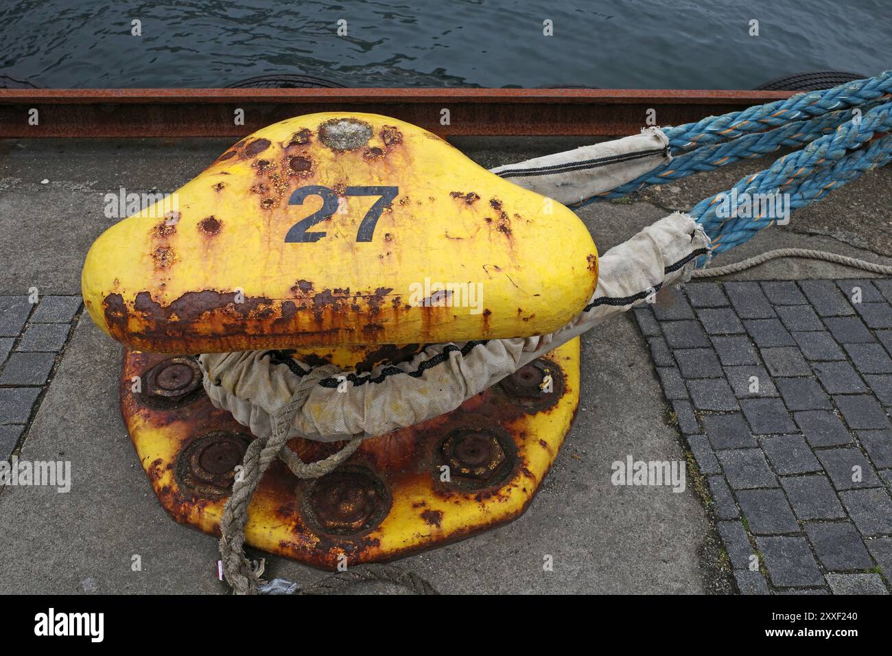 Verrosteter gelber Schiffspoller mit dem Seil eines Schiffes. Es ist Schiffspoller Nummer 27 Stockfoto