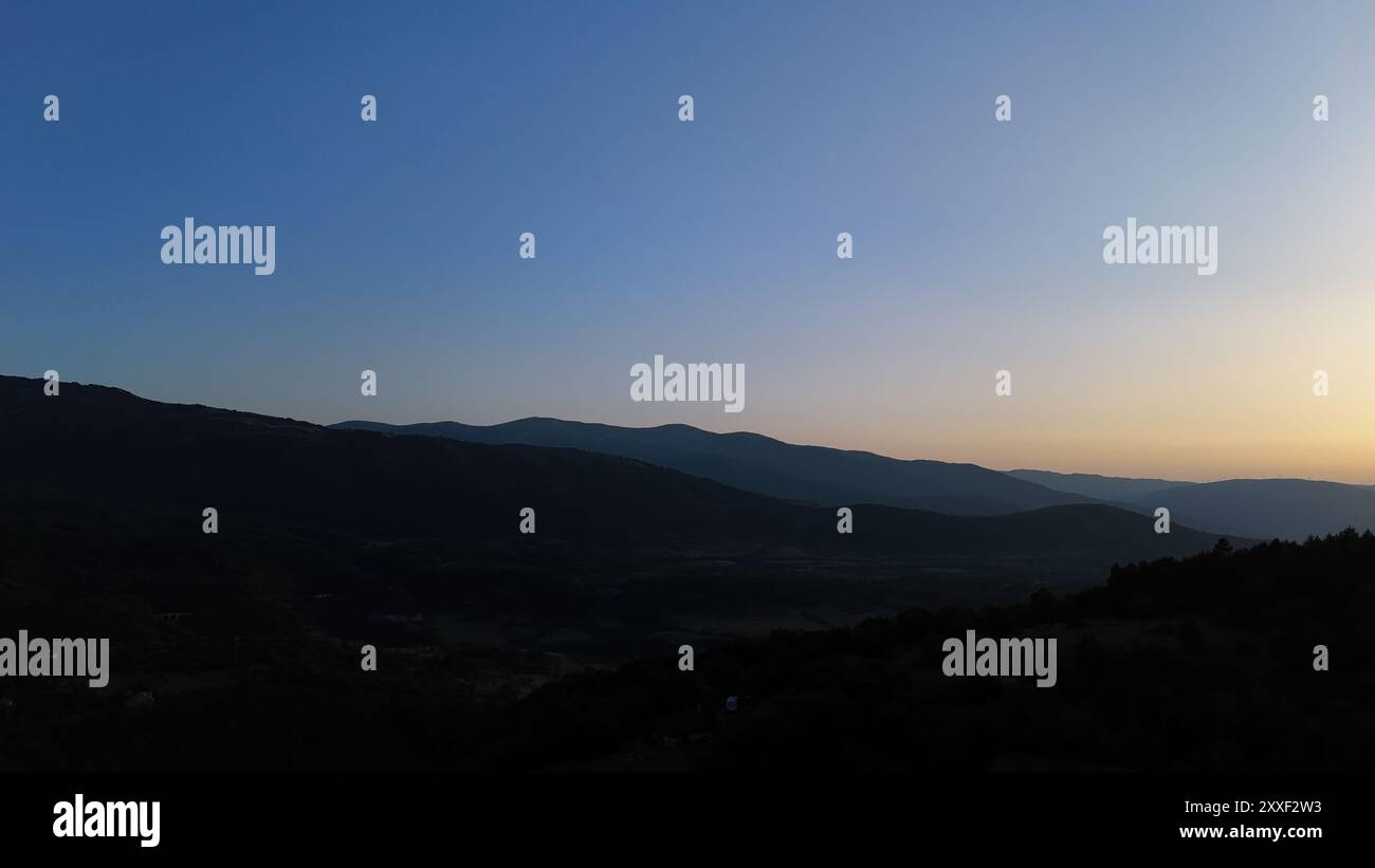 Während der Tag in die Nacht übergeht, zeichnen sanfte Farbtöne den Himmel über hügeligen Hügeln und laden zur Besinnung und Ruhe in der Umarmung der Schönheit der Natur ein. Stockfoto