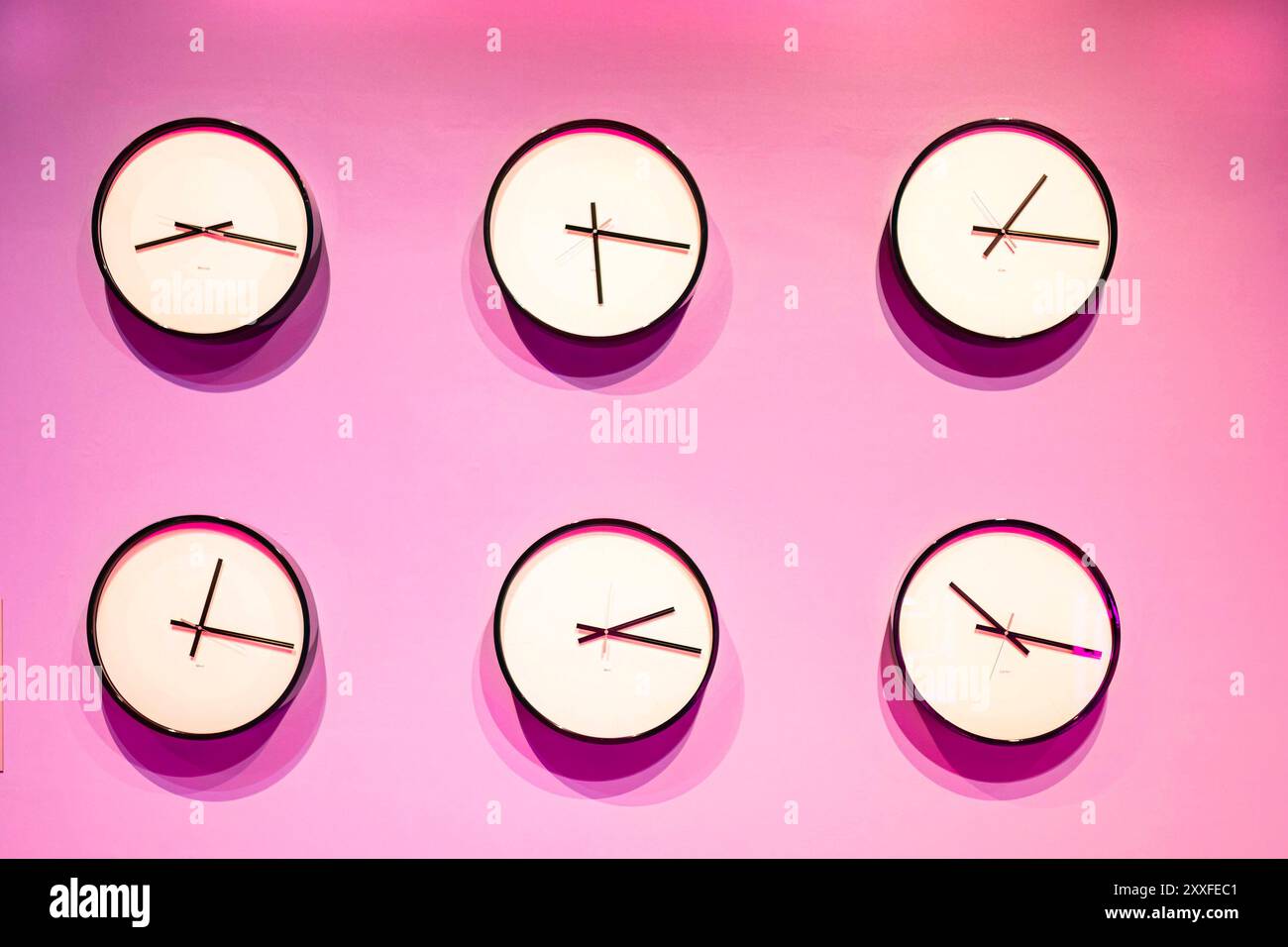 Sechs analoge Wanduhren mit unterschiedlichen Uhrzeiten auf einem leuchtend rosa Hintergrund. World Time Zone Concept Stockfoto