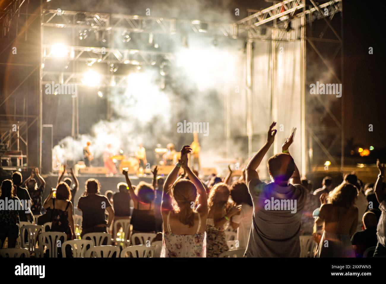 Ein lebhaftes Rockkonzert im Freien bei einer begeisterten Menschenmenge, die Live-Musik und lebhafte Atmosphäre unter den Bühnenlichtern genießt. Stockfoto