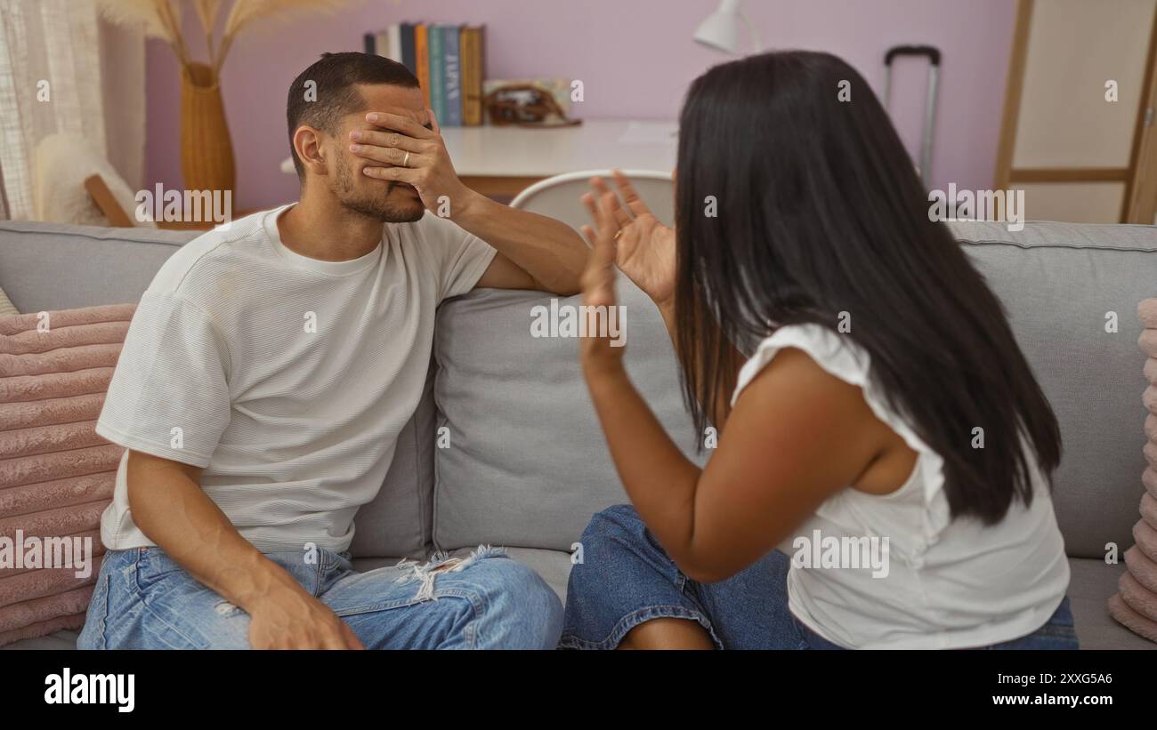 Ein Paar streitet in einem Wohnzimmer, während ein Mann sein Gesicht mit der Hand bedeckt, während eine Frau emotional Gesten zeigt und einen angespannten Moment in einem Domesti hervorhebt Stockfoto