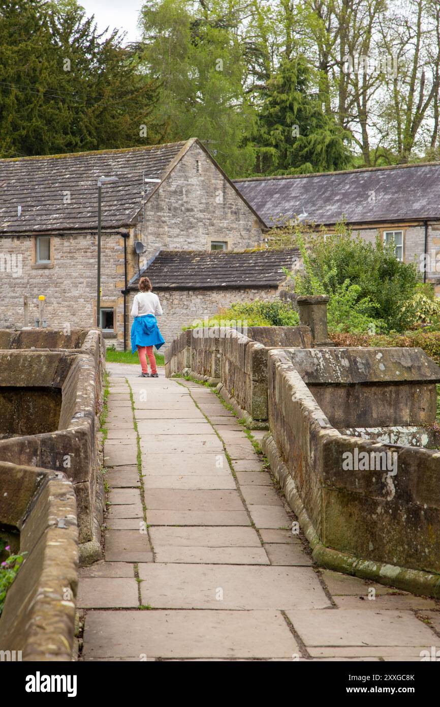 Frau, die über die Holme Bridge geht, die alte mittelalterliche Steinbrücke über den Fluss Wye in der Marktstadt Bakewell im Peak District Derbyshire Stockfoto