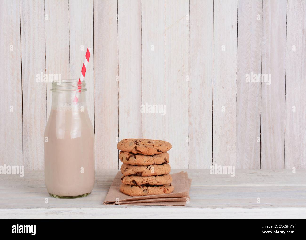 Ein Snack mit Keksen und Milch auf einem rustikalen Holzset. Eine kleine Flasche Schokoladenmilch mit einem Trinkhalm und einem Stapel Schokoladenchips-Kekse. Horiz Stockfoto