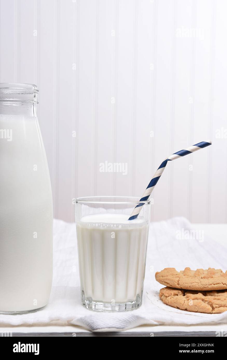 Ein Snack mit Milch und Plätzchen auf einem weißen Tisch mit weißer Wand. Das Glas hat einen Drink Strohhalm mit Keksen an der Seite. Stockfoto