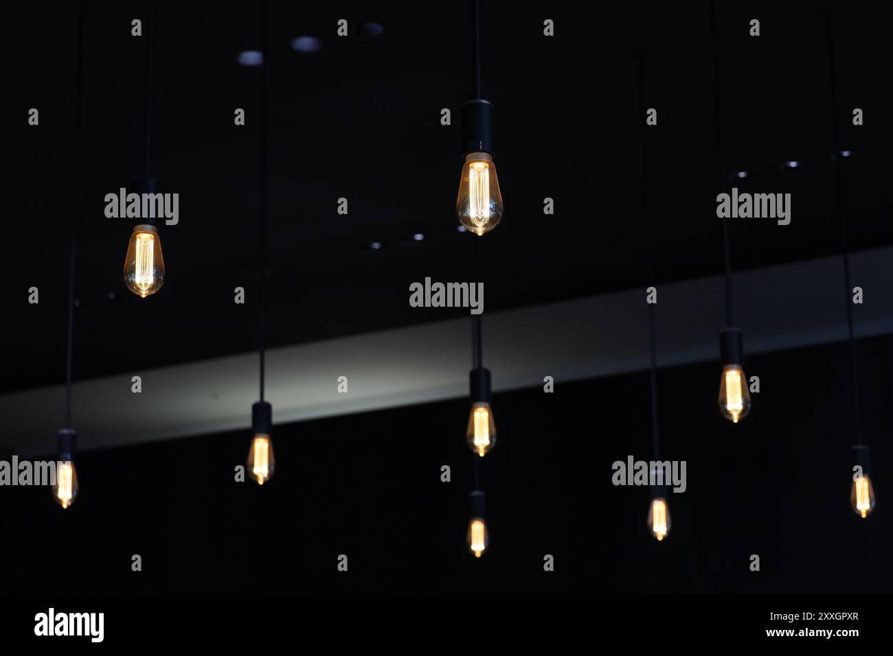 Mehrere einfach gestaltete Pendelleuchten hängen von der Decke in einem schwach beleuchteten Raum Stockfoto