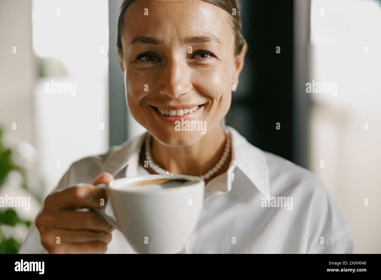 Eine lächelnde Frau genießt eine Tasse Kaffee in einem modernen und einladenden Ambiente Stockfoto