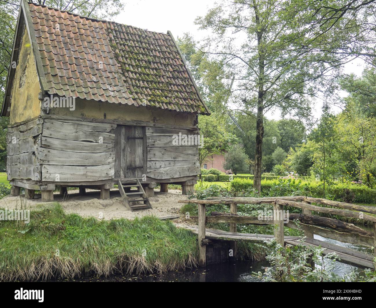 Alte Holzhütte mit moosbedecktem Dach am Ufer eines kleinen Baches, umgeben von dichter Vegetation, Bad Zwischenahn, ammerland, deutschland Stockfoto