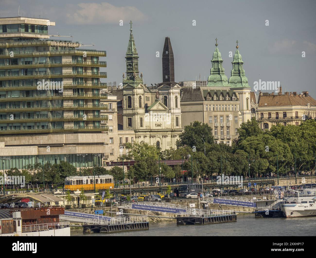 Blick auf eine Stadt mit modernen und historischen Gebäuden und Straßenbahnen am Fluss bei sonnigem Wetter, budapest, donau, ungarn Stockfoto