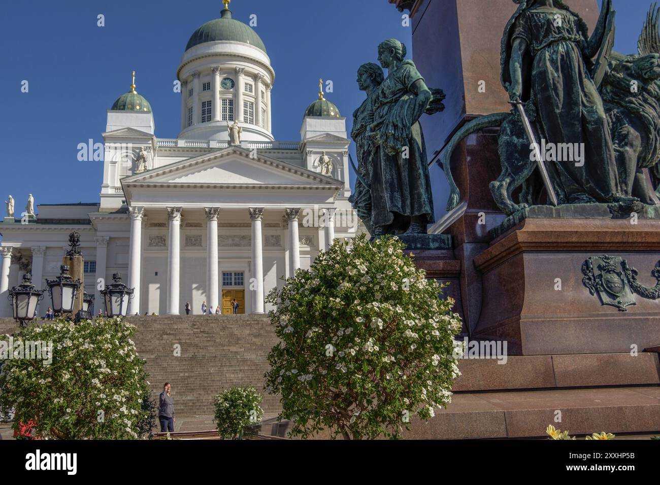 Weiße Kathedrale mit grüner Kuppel und Statue im Vordergrund, umgeben von Blumen und unter blauem Himmel, Helsinki, Finnland, Europa Stockfoto