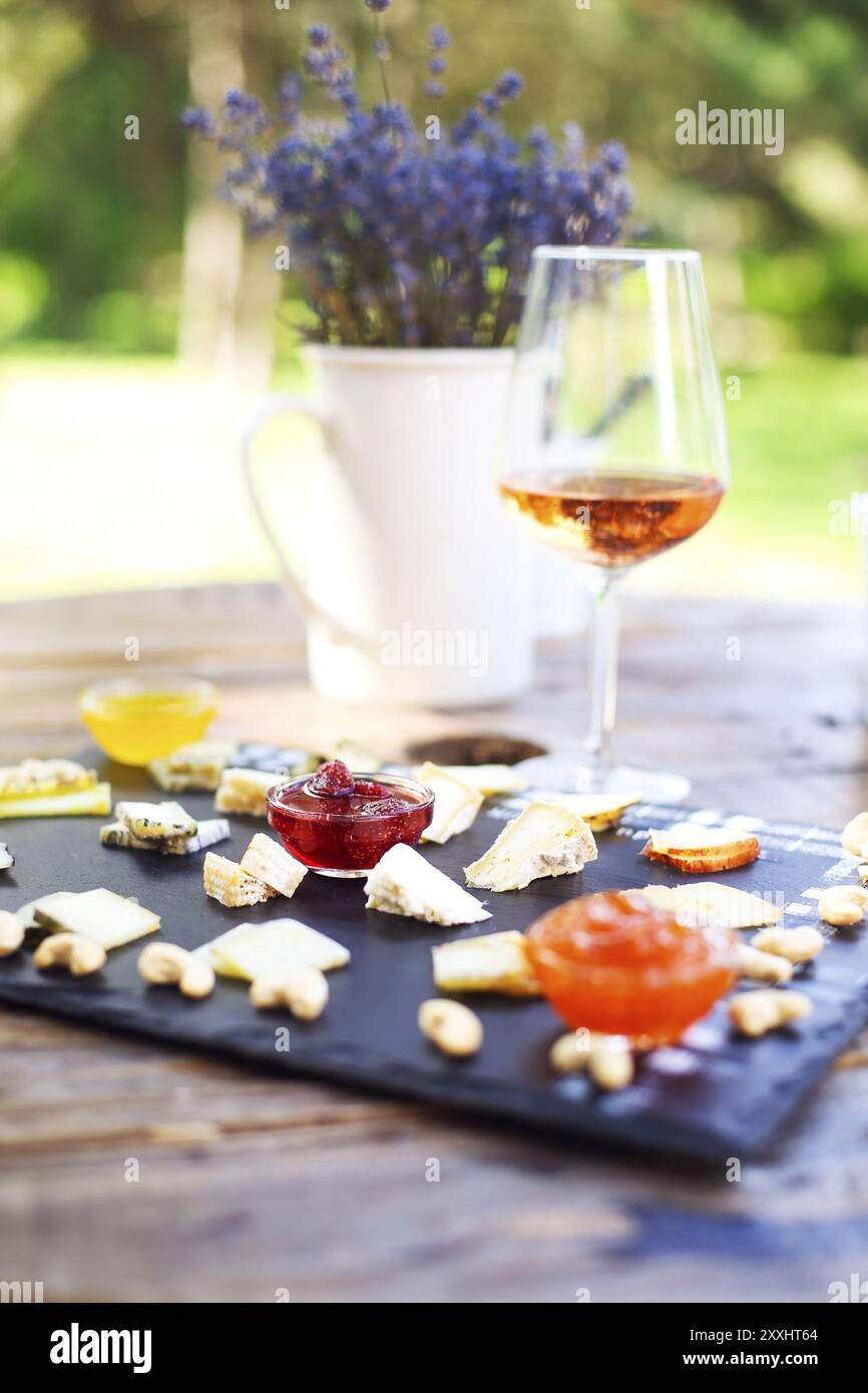 Traube, Einstellen von verschiedenen Arten von Käse mit einem Glas rosa Wein auf dem Tisch im Garten Stockfoto