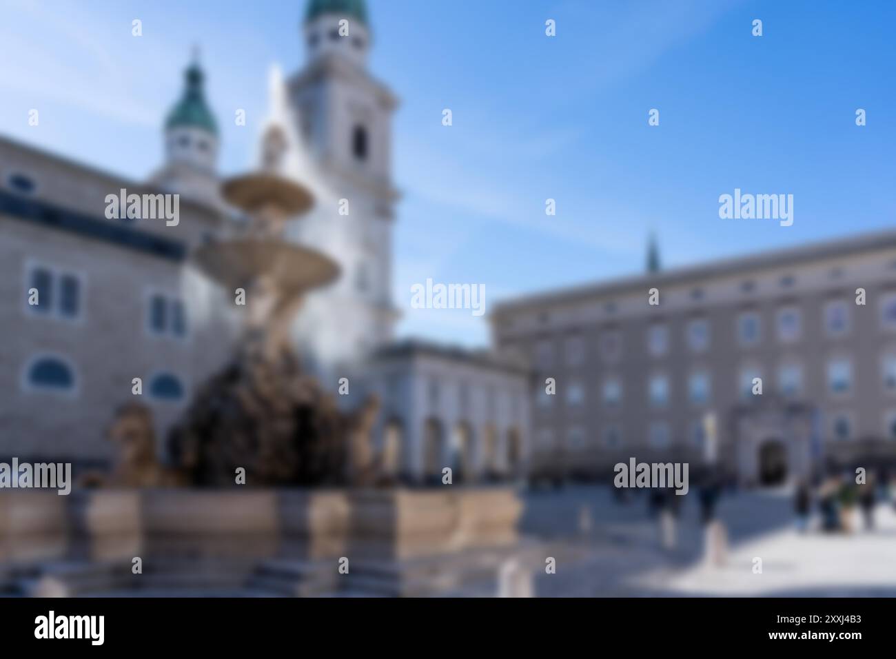 Ein verschwommenes Foto eines Brunnens in der Mitte eines europäischen Platzes. Der Brunnen ist von hohen Gebäuden und Menschen umgeben. Der Himmel ist klar blau. Stockfoto