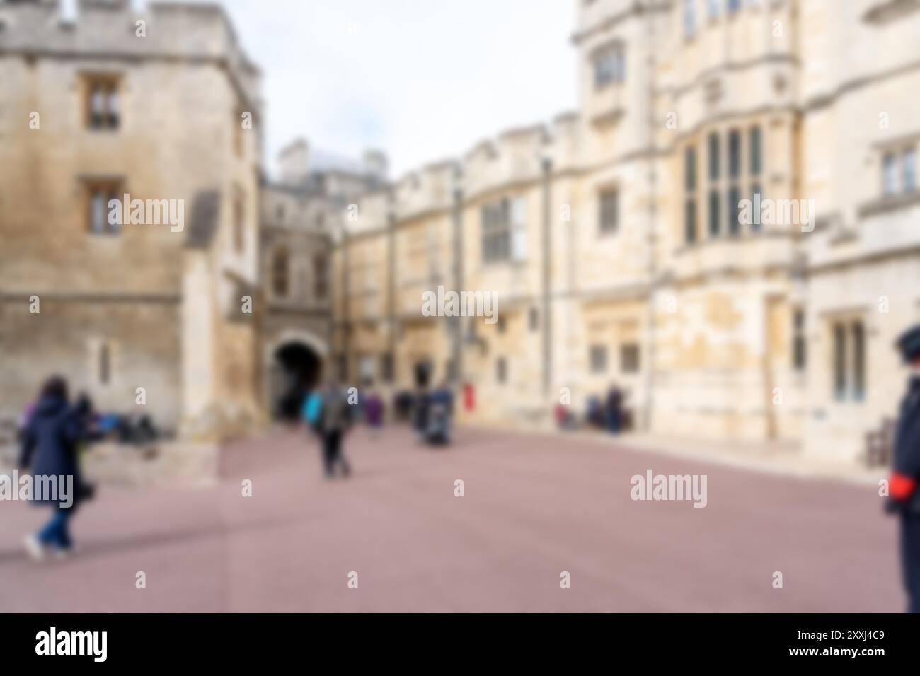 Ein verschwommenes Foto von einem Innenhof aus Stein mit Menschen, die durch einen großen Torbogen laufen. Das Foto zeigt einen Bokeh-Hintergrund und die Gebäude hinten Stockfoto