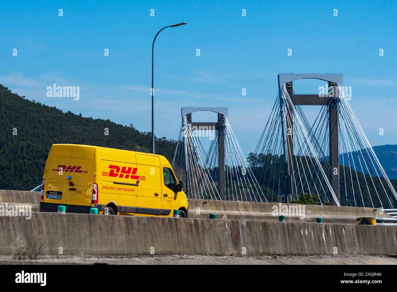 Vigo, Pontevedra, 6.18.2024; Paketlieferwagen mit dem Bild des DHL-Unternehmens, das auf der Autobahn über die Rande-Brücke in Vigo verkehrt. Stockfoto