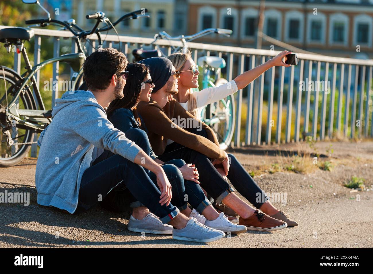 Zeit für Selfie. Gruppe junger lächelnder Menschen, die sich aneinander binden und Selfie machen, während sie draußen mit Fahrrädern sitzen Stockfoto