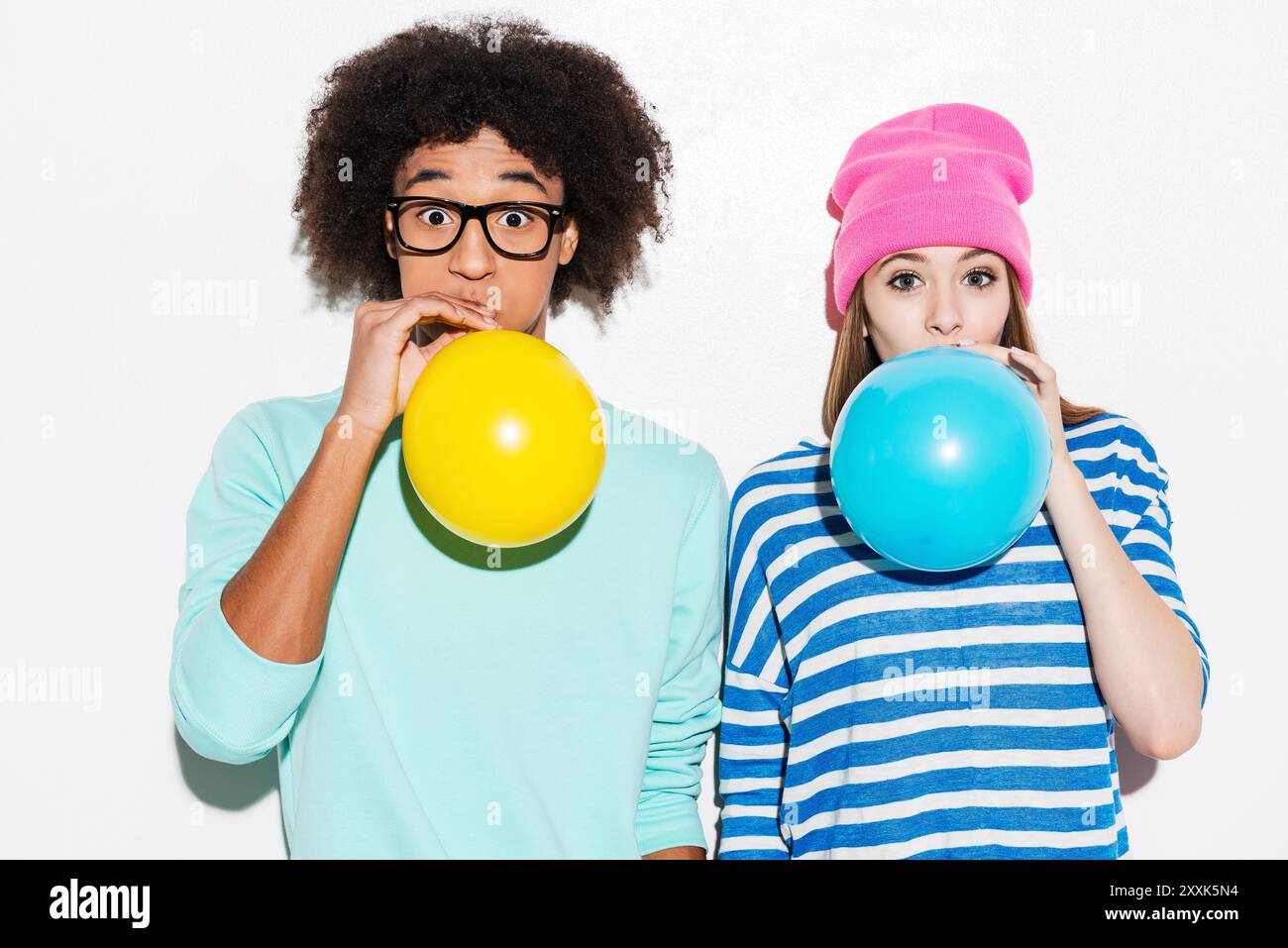 Doppelte Bubble Love. Funkiges junges Paar, das Ballons aufbläst, während es vor weißem Hintergrund steht Stockfoto