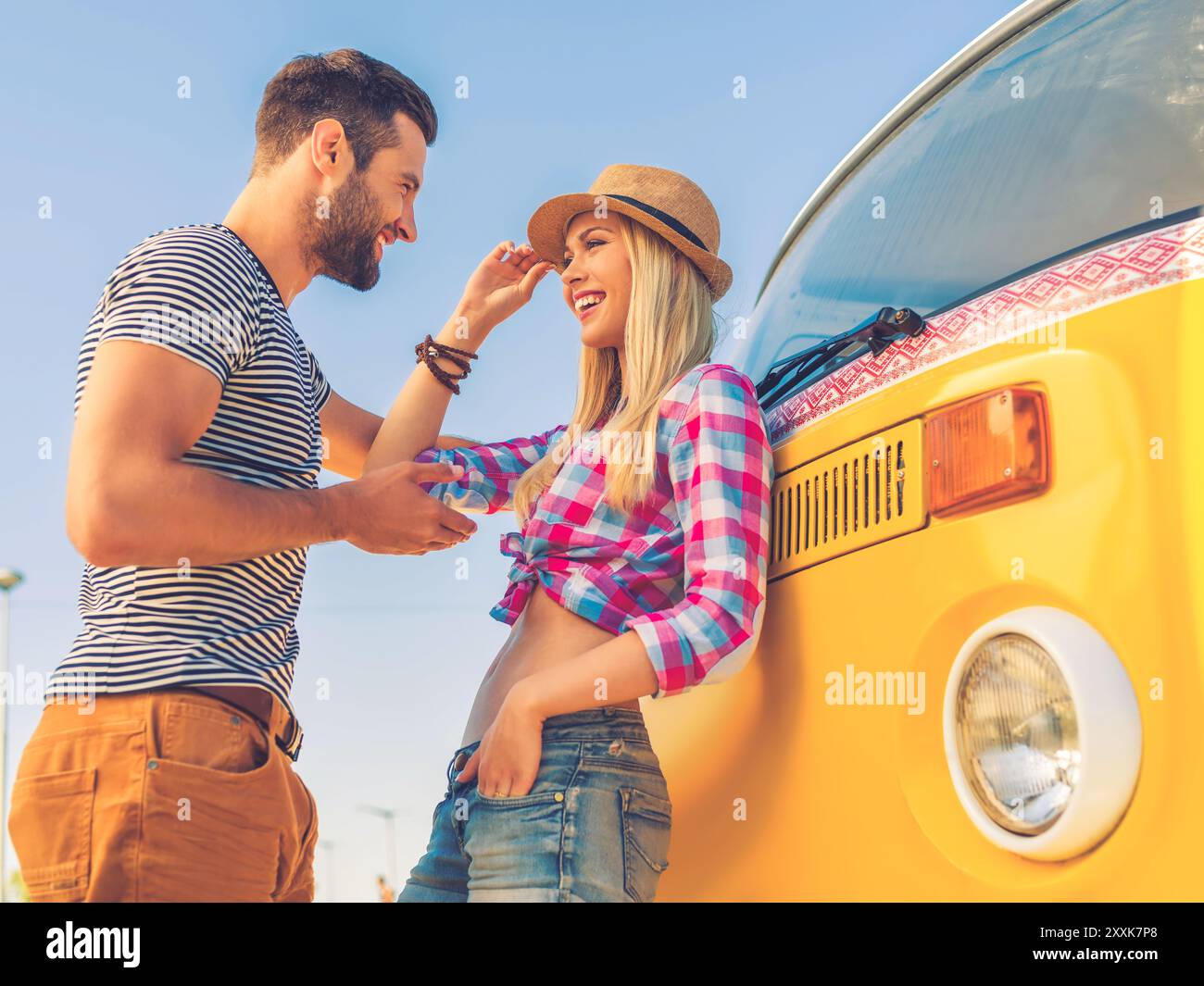Jung und sorglos. Niedriger Blickwinkel auf ein wunderschönes junges Paar, das miteinander spricht und lächelt, während er sich an ihren Retro-Kleinbus lehnt Stockfoto