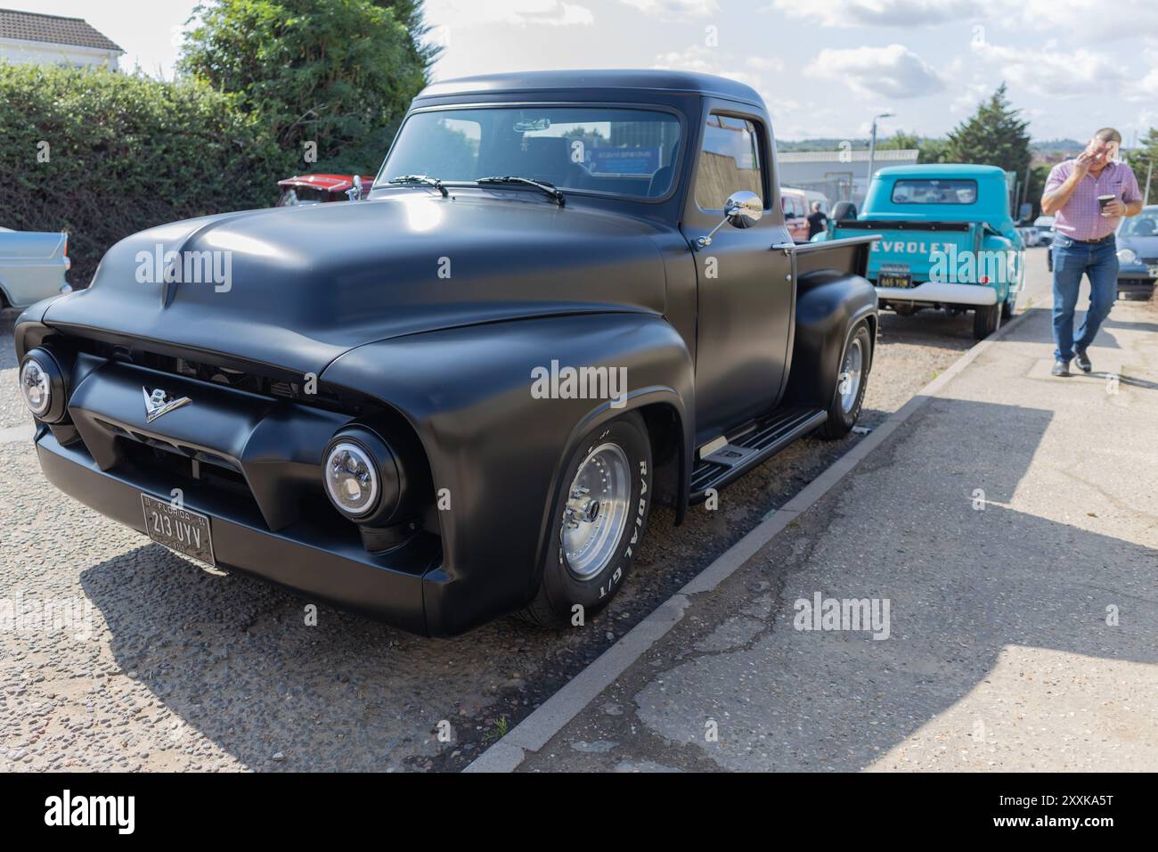 Rayleigh, Großbritannien. August 2024. Ein mattschwarzer Ford Pickup-Truck aus den 1950er Jahren und ein türkisfarbener Chevrolet-Truck parken am Straßenrand bei einem Treffen mit einem klassischen Fahrzeug. Die Szene fängt Retro-Styling, Kontraste der Restauration und das öffentliche Interesse an der amerikanischen Automobilgeschichte ein. Ein Fußgänger spaziert in der Nähe, was ein Gefühl von ungezwungenem urbanem Leben verleiht. Amerikanisches Auto und Truck treffen sich in der Farm Fresh Garage. Bei der Veranstaltung können die Besitzer ihre Fahrzeuge mitbringen, damit die Besucher einen Blick aus der Nähe werfen können. Penelope Barritt/Alamy Live News Stockfoto