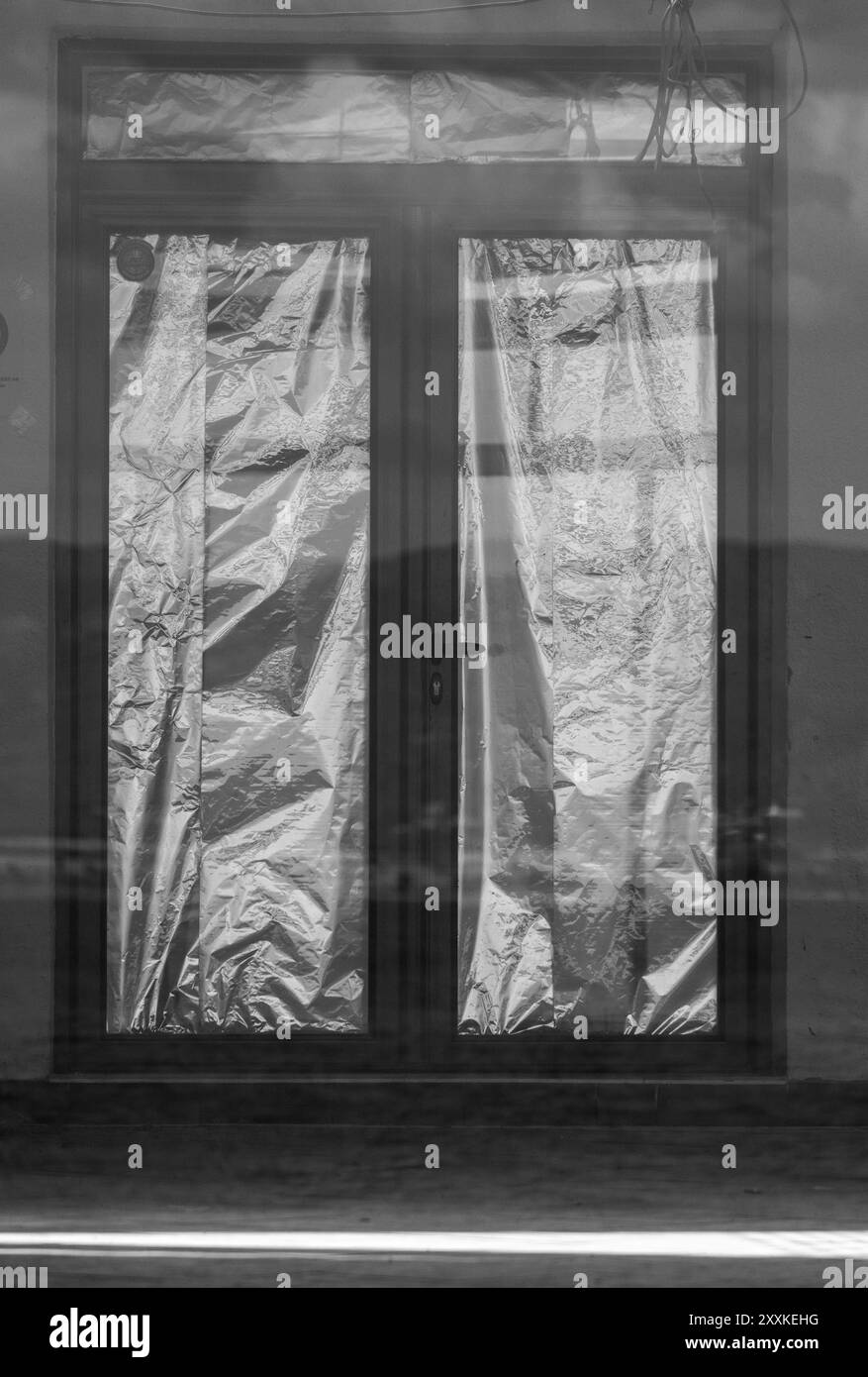 Schwarze Eingangstür mit Folie: Reflexion in Glas und Sonnenlicht auf dem Boden. Einfarbige Details. Stockfoto