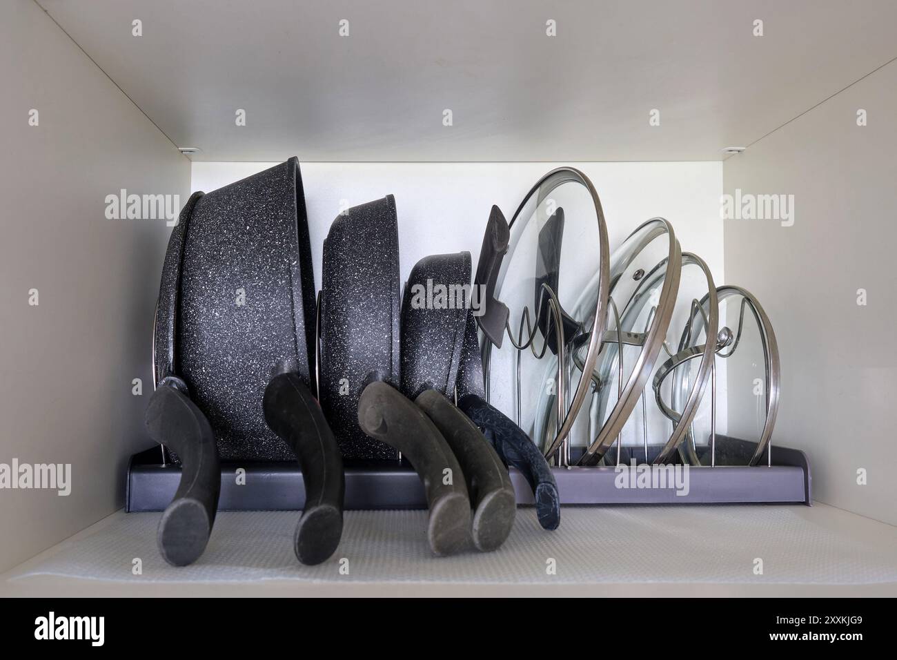 Ordnung der Bestellung von Geschirr, Töpfen und Pfannen in der Küche. Der Prozess der Verwendung von Töpfen und Deckeln in einem Küchenschrank Stockfoto
