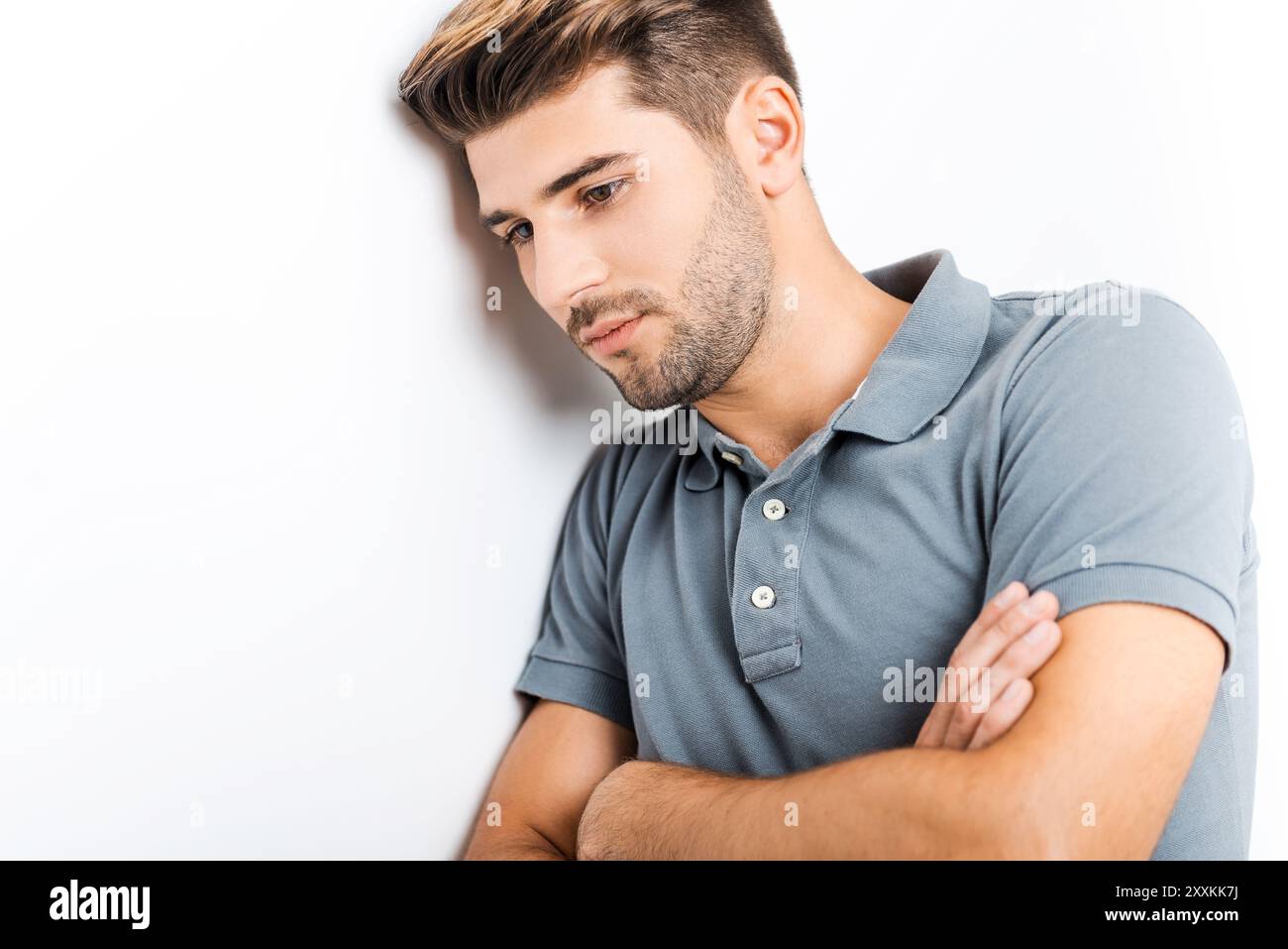 In Gedanken verloren. Nachdenklicher junger Mann, der die Arme überkreuzt und wegblickt, während er sich an die Wand lehnt Stockfoto