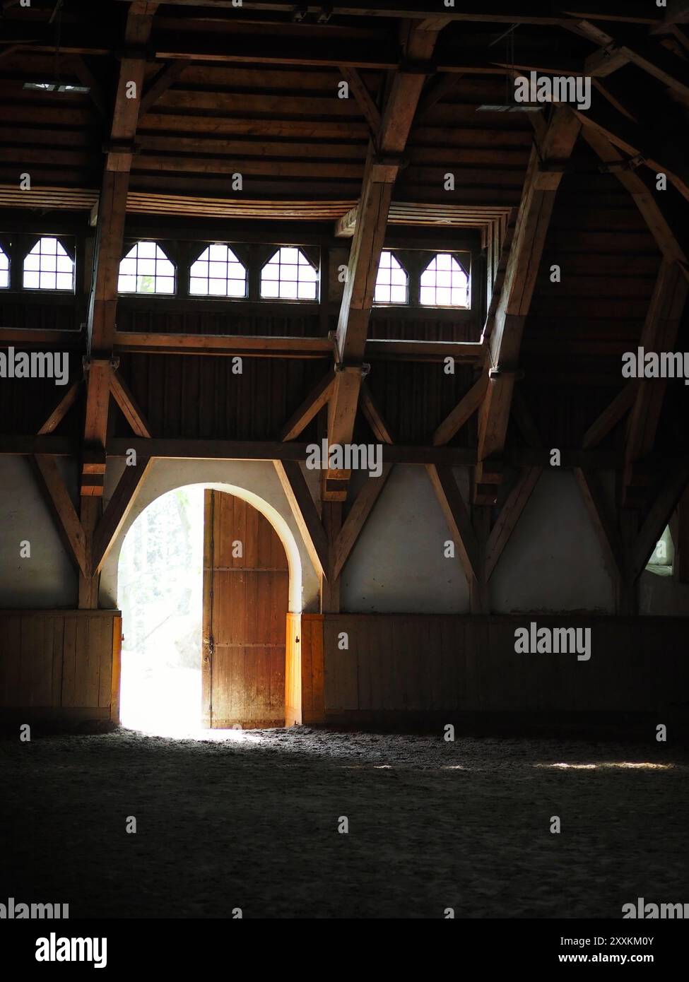 Sonnenlicht strömt durch eine bogenförmige Tür in eine rustikale Holzscheune mit bogenförmigen Balken und schafft eine ruhige und ruhige Szene aus Licht und Schatten Stockfoto