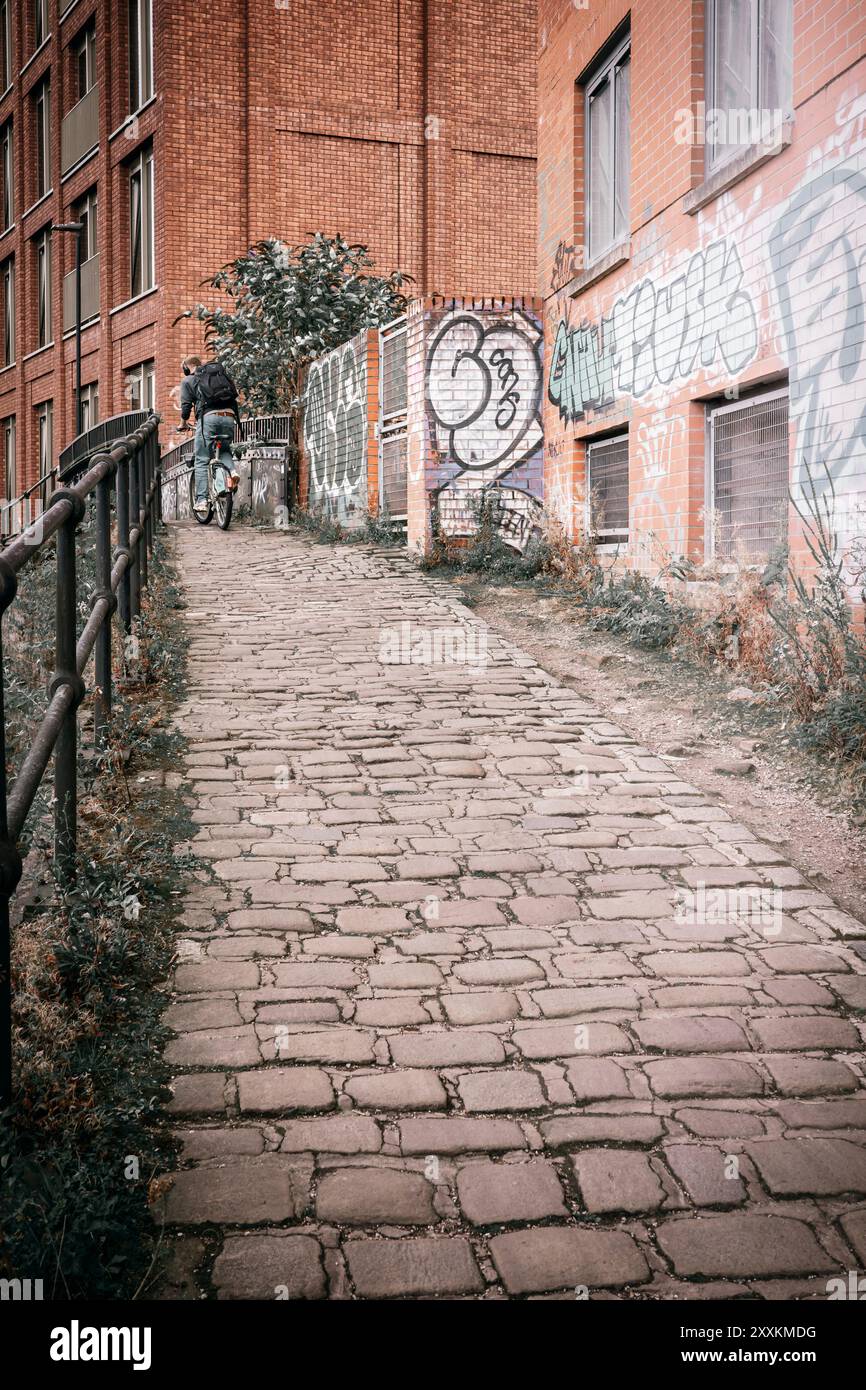 Manchester, Greater Manchester, Großbritannien. 24. August 2024: Ein Radfahrer wird auf einem steilen Kopfsteinpflasterweg in einer urbanen Umgebung gefangen. Die Szene ist Ado Stockfoto
