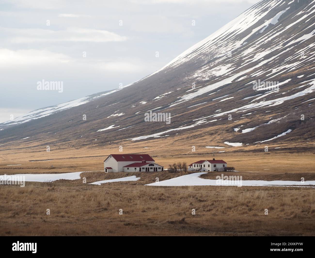 Zwei Bauernhäuser mit roten Dächern stehen isoliert in einem Hochland-Tal mit Schneebesen auf dem Boden und Hügeln, unter einem bewölkten Himmel, die ein heiteres Ru verkörpern Stockfoto