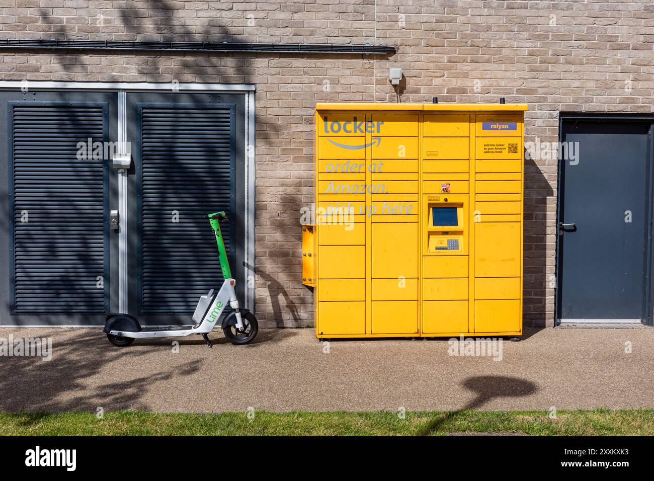 Salford, Greater Manchester, Großbritannien. 24. August 2024: Ein gelbes Schließfach neben einem geparkten Elektroroller vor einer modernen Ziegelmauer. Stockfoto