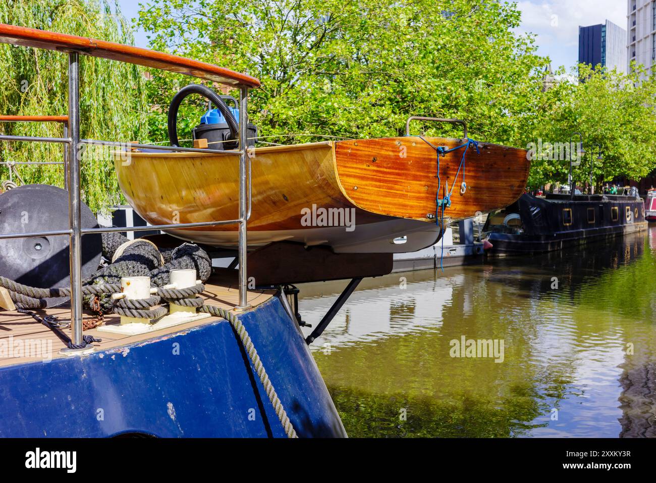 Manchester, Greater Manchester, Großbritannien. 24. August 2024: Ein elegantes Holzboot auf dem Deck eines blauen Schiffes, das an einem von Bäumen gesäumten Kanal angedockt ist. Stockfoto
