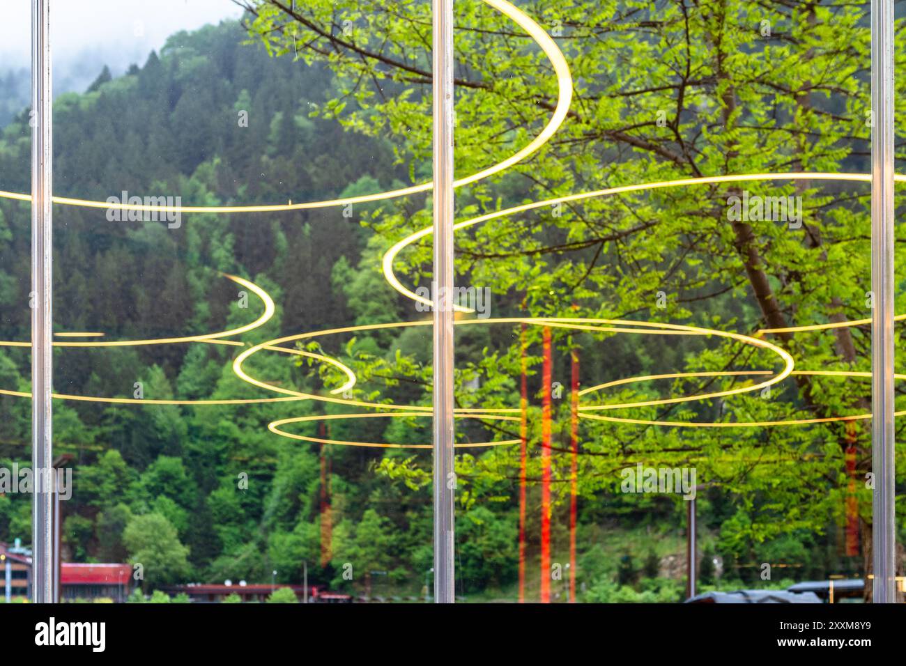 Reflexionen von Lampen in Glasfenstern und bewaldeten Berghängen im Hintergrund an bewölktem Sommertag im Dorf Uzungol am Ufer des Usungol-Sees in C Stockfoto