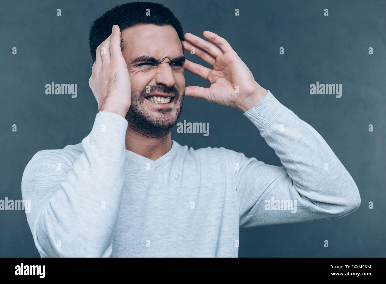 Was ist das?! Frustrierter junger Mann, der Negativität ausdrückt, während er gestickt und vor grauem Hintergrund steht Stockfoto