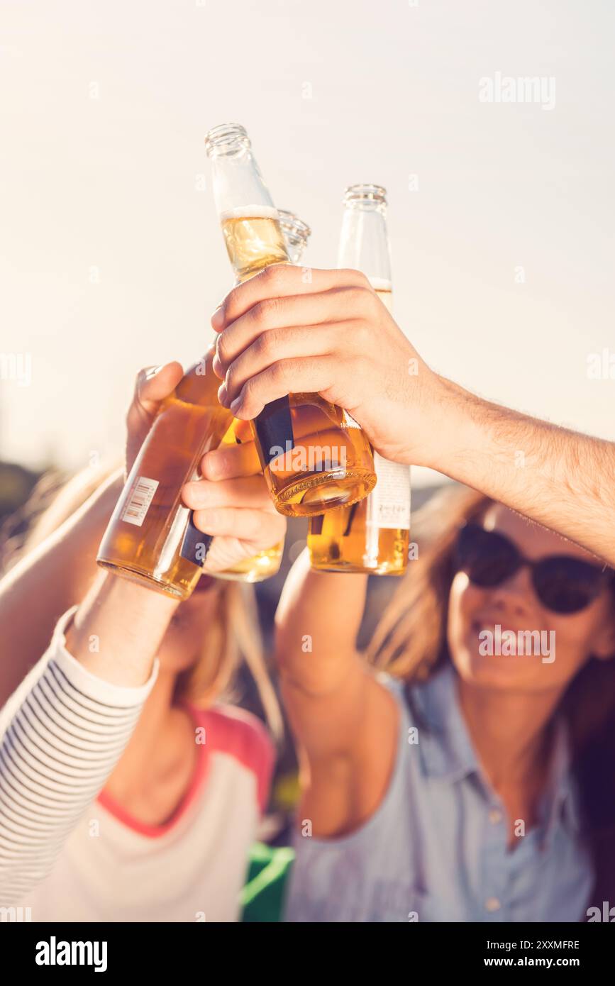 Bierzeit! Nahaufnahme von jungen, fröhlichen Leuten, die mit Bier bejubelten, während sie zusammen draußen sitzen Stockfoto