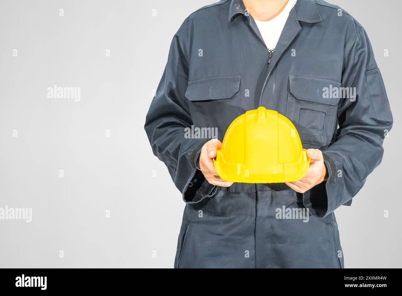 Verstopft Arbeiter, der in blauer Umhüllung steht und gelben Hardhut hält Isoliert auf grauem Hintergrund Stockfoto