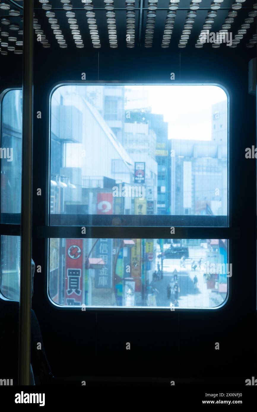 Blick auf eine geschäftige japanische Stadt durch das Fenster eines öffentlichen Verkehrsmittels, mit Schildern und Fußgängerverkehr darunter Stockfoto