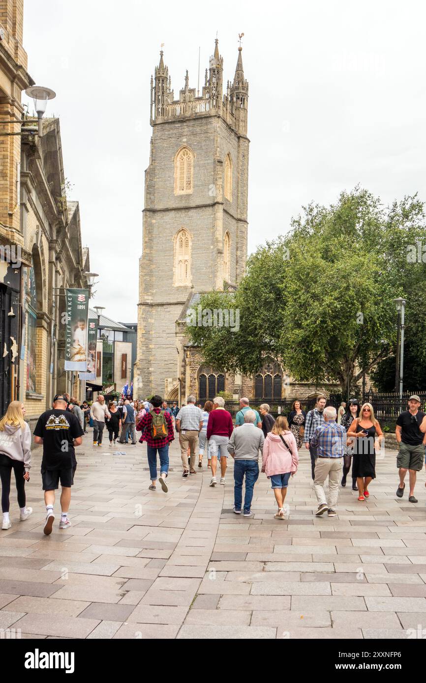 Einkaufsmöglichkeiten und Touristen entlang der Trinity Street in der walisischen Hauptstadt Cardiff mit Blick auf die St. John the Baptist City Parish Church. Stockfoto