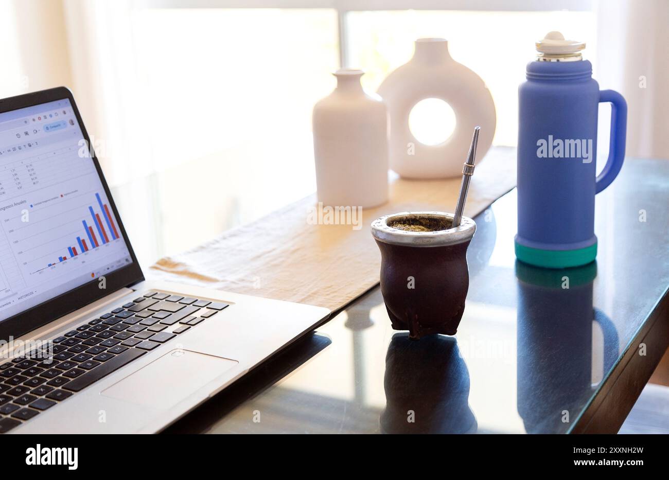 Arbeite und trinkende Yerba Mate. Kürbis-Mate mit Yerba innen, über dem Tisch neben einem Laptop am Arbeitsplatz. Stockfoto