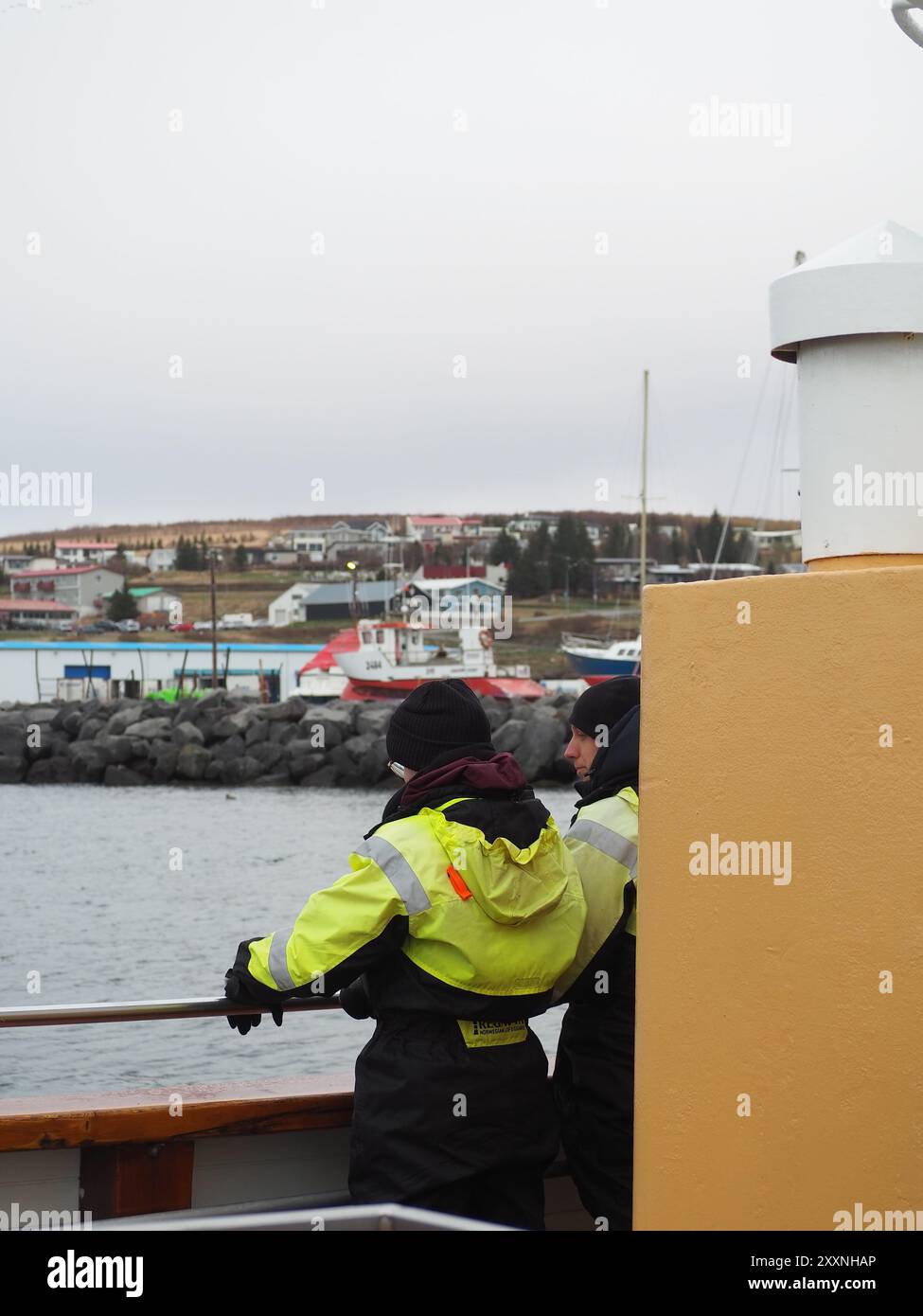 Husavik, Island - 12. Mai 2024: Menschen in hellen Überlebensanzügen stehen auf einem Boot, während es durch ein kaltes, graues Meer segelt, und symbolisieren menschliche Widerstandsfähigkeit und Stockfoto