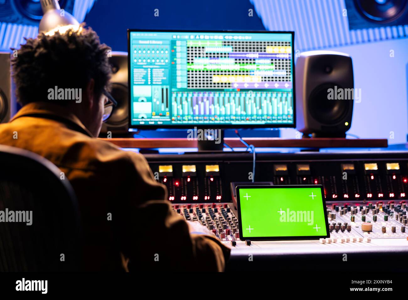 afroamerikanischer Audioproduzent, der Tasten und Schieberegler drückt, Mockup-Display im professionellen Musikstudio. Sound Designer, der Titel bearbeitet und Lautstärkepegel anpasst, motorisierte Fader. Stockfoto