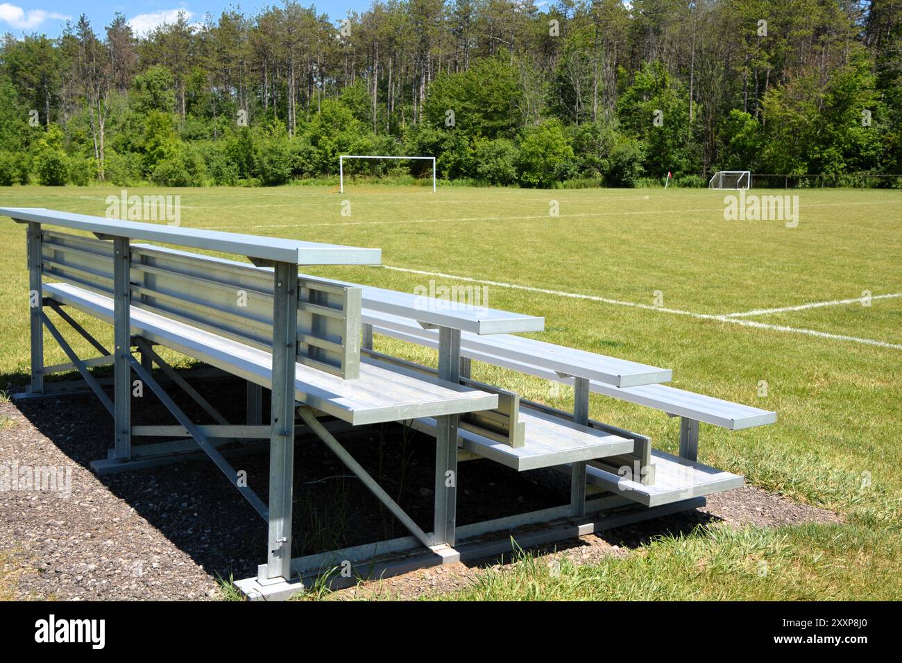 An einem sonnigen Sommertag sitzen auf einem Fußball- und Sportplatz leere Bleachsen aus Aluminium. Stockfoto