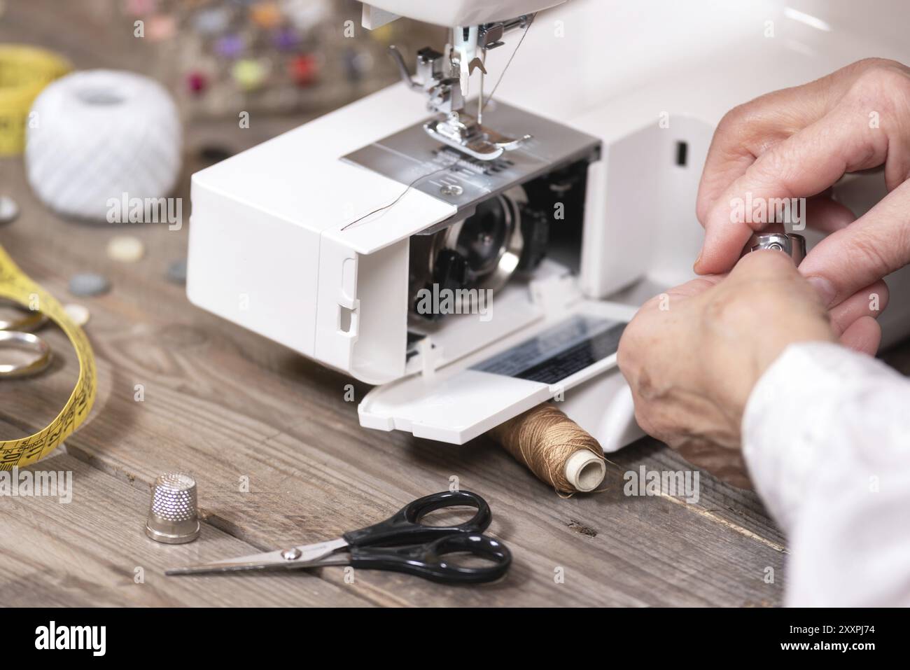 Nahaufnahme der Näherin Hände, die den Spulenkoffer entfernen, um die Wartung einer elektrischen Nähmaschine zu erledigen Stockfoto