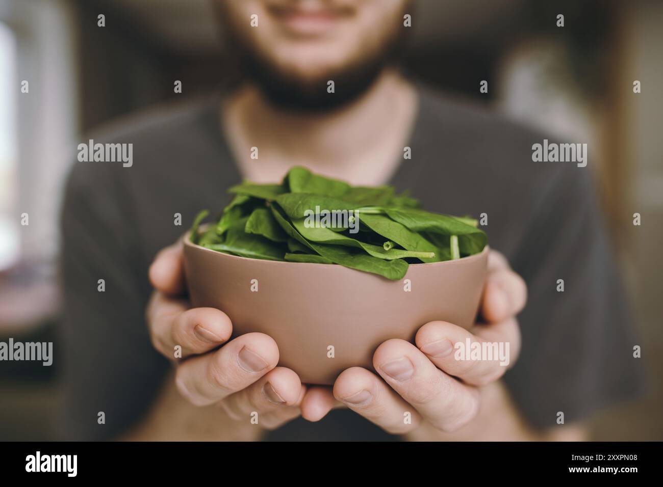 Hände lächelnder Mann hält frische grüne Salatblätter Spinat auf verschwommenem Hintergrund. Gesunde vegetarische Ernährung Konzept. Grüne Blätter von Spinat. Gi Stockfoto