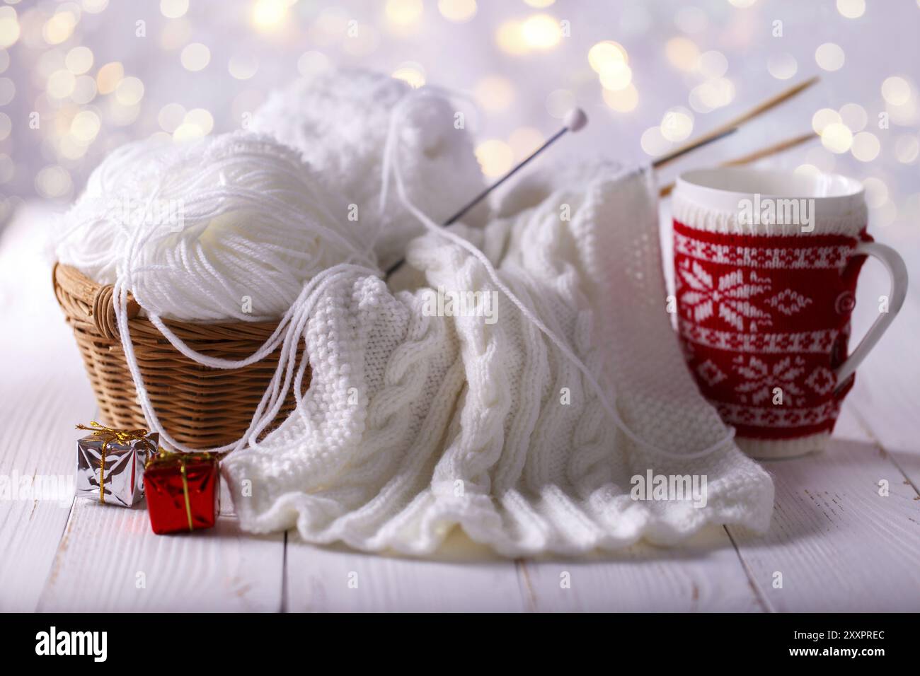 Kugeln aus weißem Garn in einem Korb mit Stricknadeln und Tasse Kaffee auf Holz- Hintergrund Stockfoto