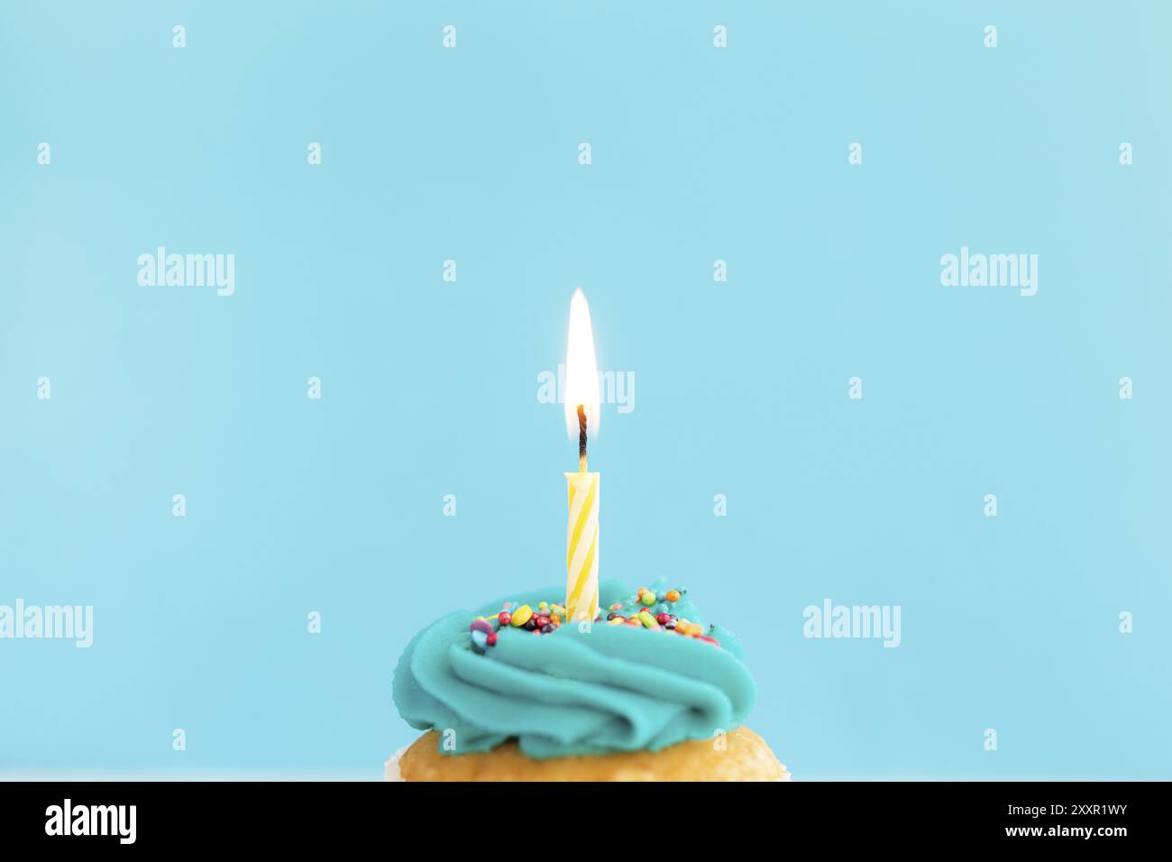 Geburtstagsgrußkonzept. Brennende Kerze auf einem Muffin oder Cupcake. Blauer Hintergrund Stockfoto