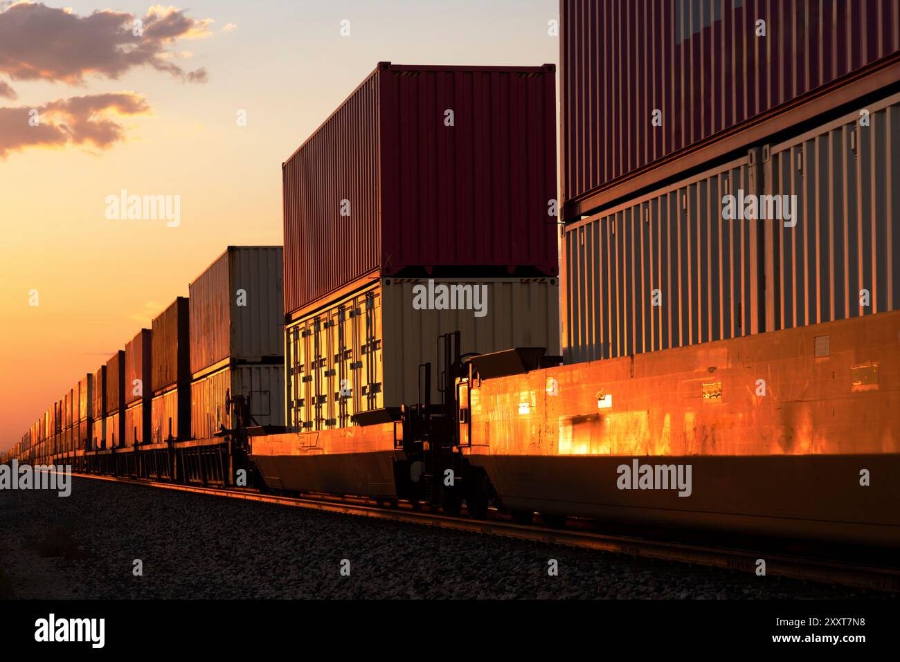 Das rote Leuchten des Sonnenuntergangs auf einem vorbeifahrenden Containerzug Stockfoto