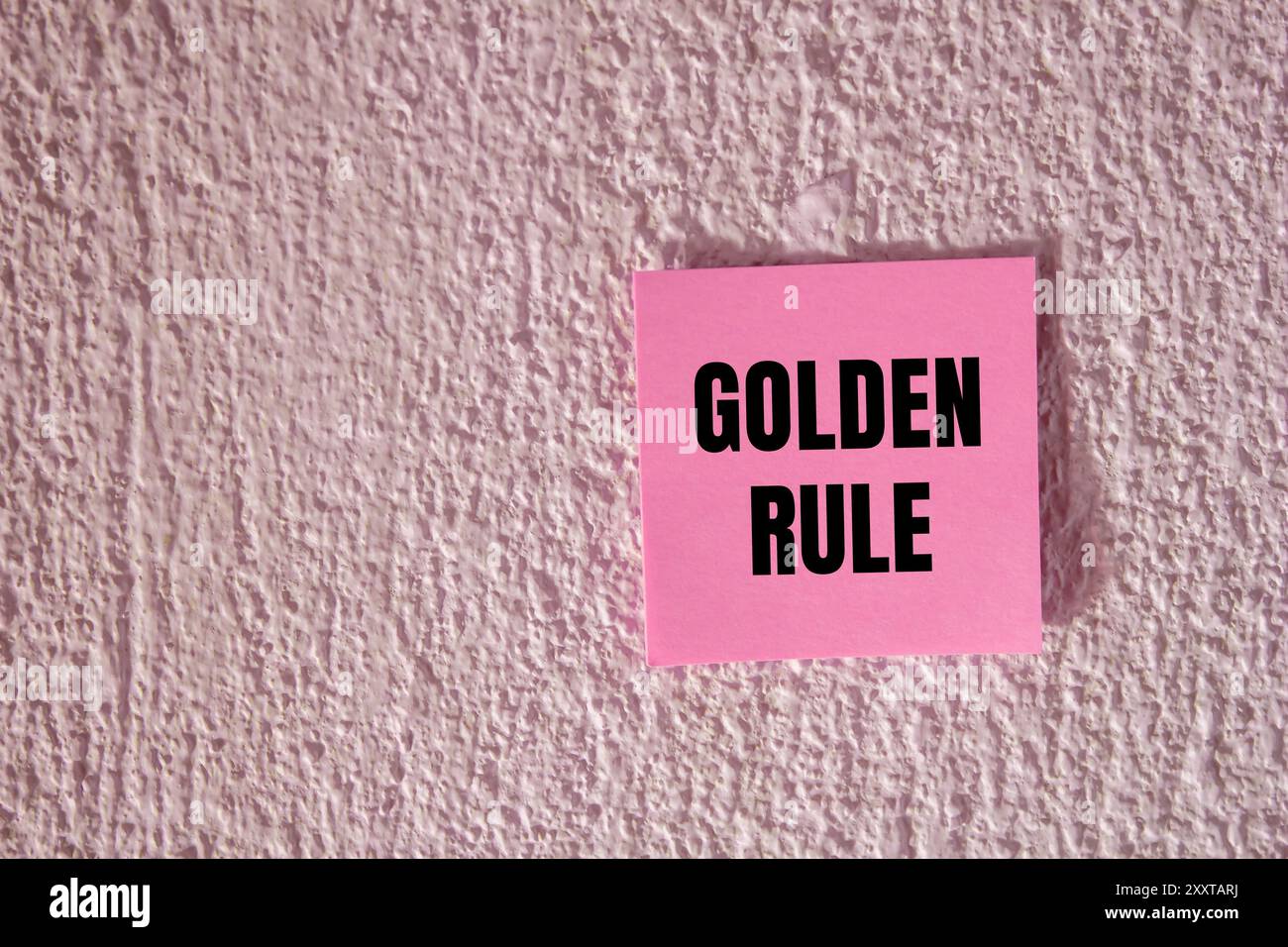 Goldene Regel-Nachricht auf rosa Papier auf Betonwand Hintergrund geschrieben. Konzeptionelles goldenes Regelsymbol. Kopierbereich. Stockfoto
