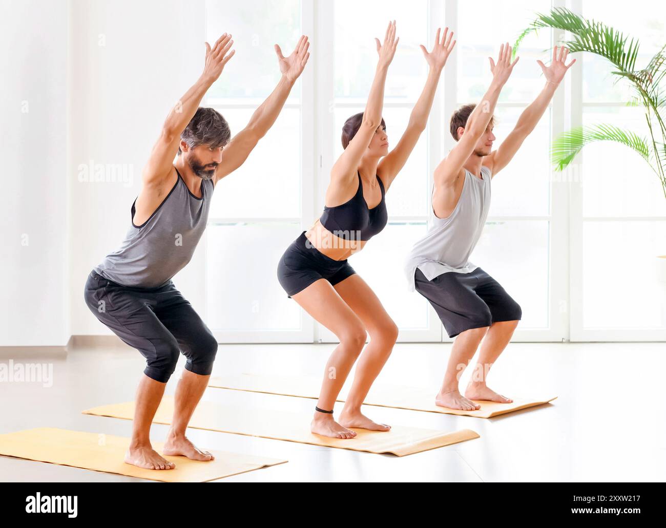 Gruppe von Menschen, die beim Üben Utkatasana oder Stuhl Pose machen Yoga im hellen und geräumigen Fitnessraum Stockfoto