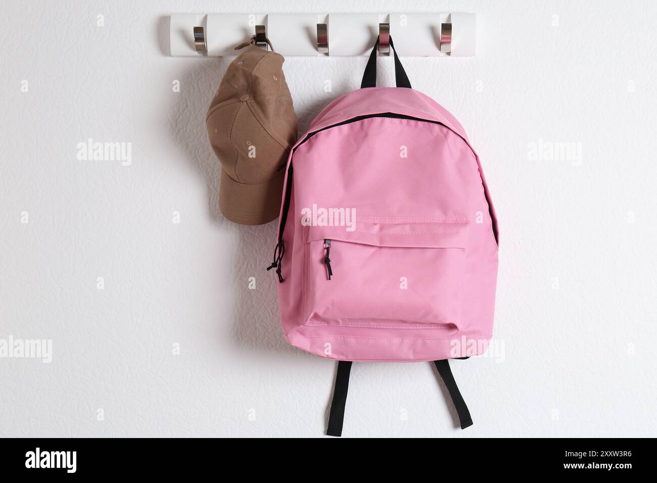 Rosafarbener Rucksack und Mütze hängen an der weißen Wand Stockfoto