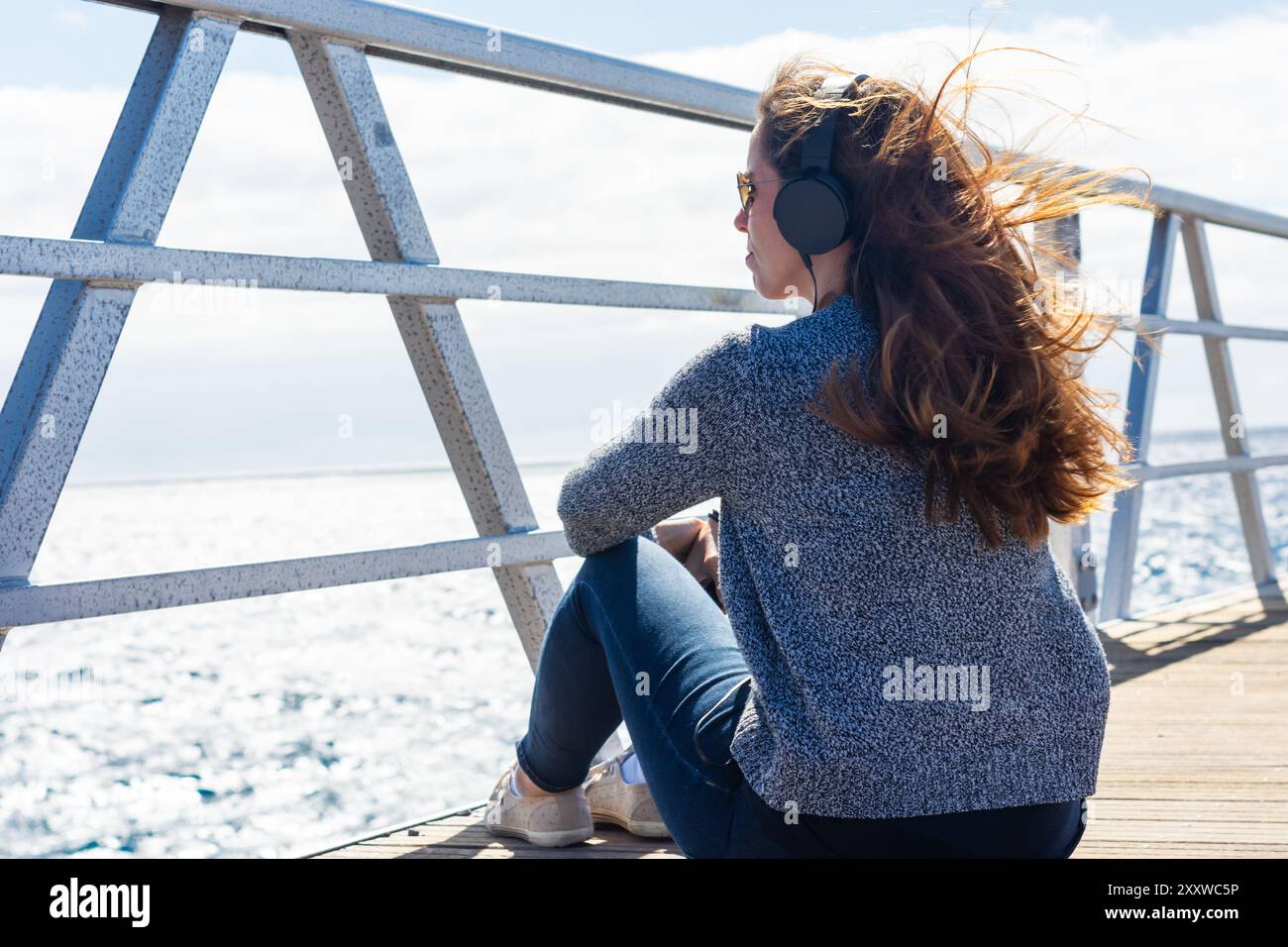 Frau, die Musik hört, mit ihrem Handy auf einer Brücke Stockfoto