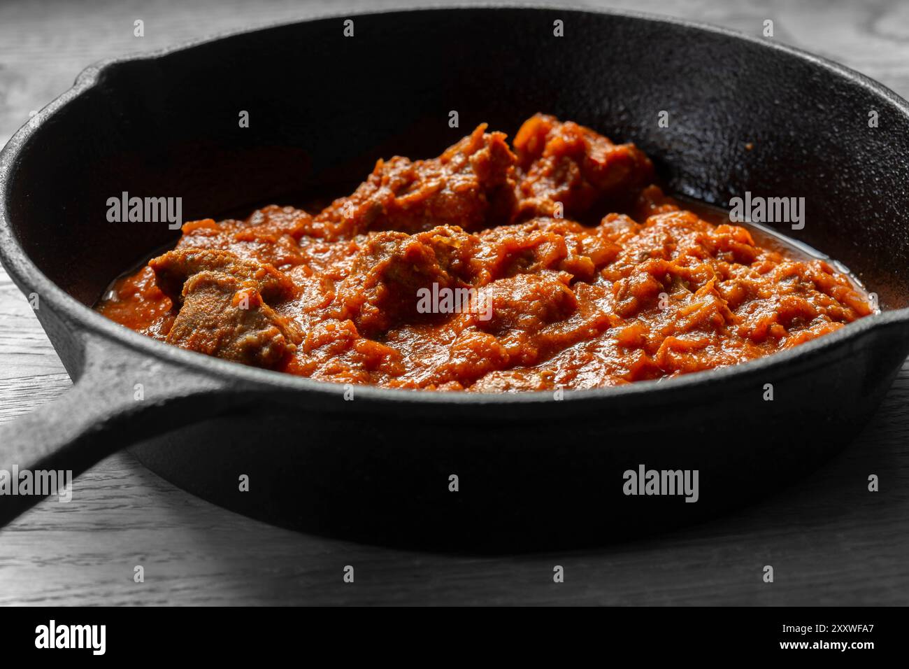 Rogan josh Lammcurry in einer gusseisernen Pfanne gekocht. Auf hölzernem Hintergrund Stockfoto